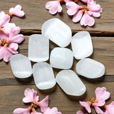 White tumbled selenite on a wooden surface with pink flowers