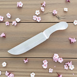 White selenite knife on a wooden surface with scattered pink flowers